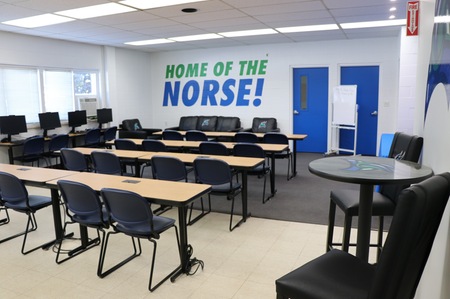 a classroom with tables and chairs, computers, and a high hat table