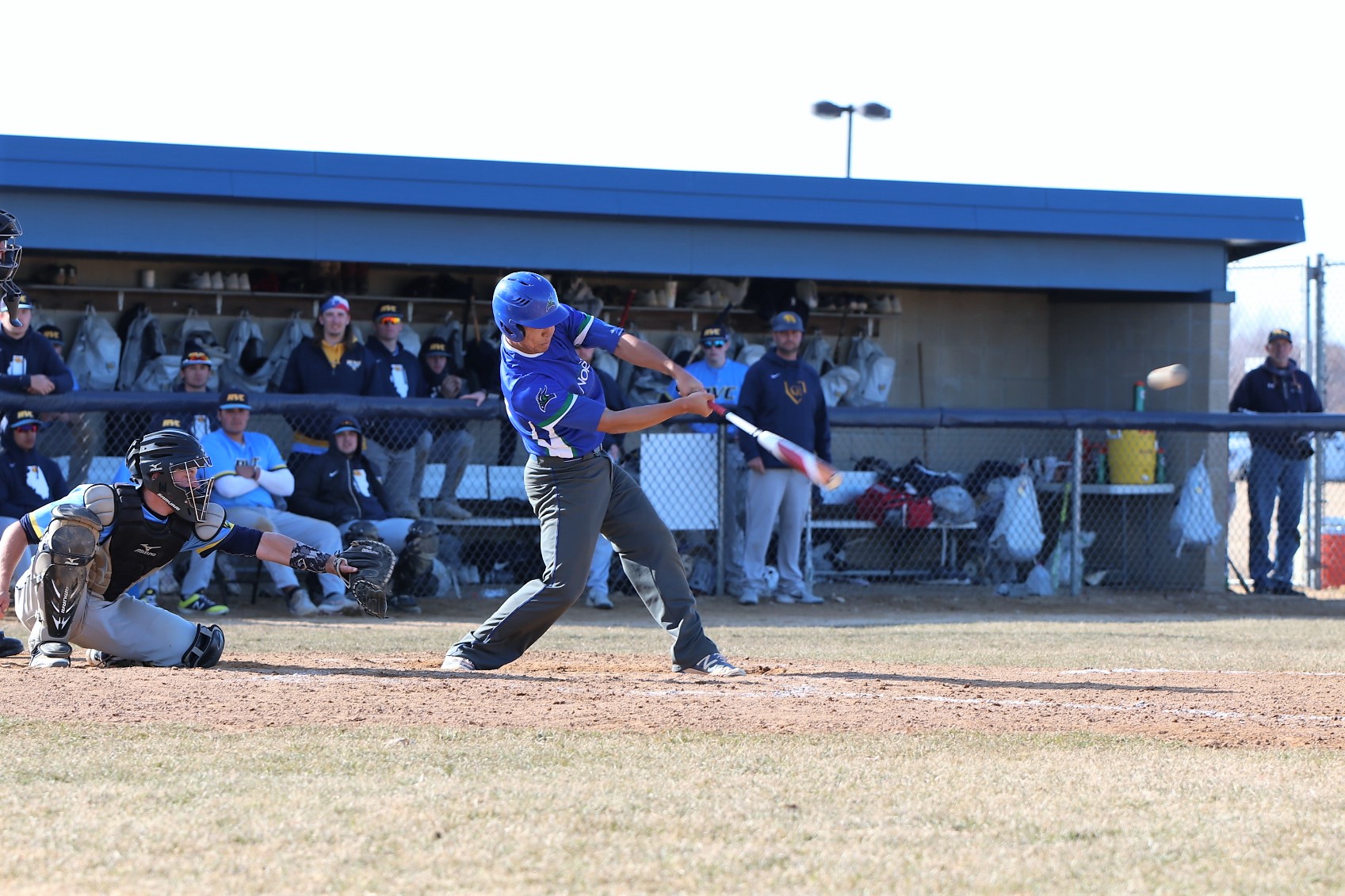 Mark Zhang in mid swing, the ball has left his bat in the air, the opposing dugout looks on from the background