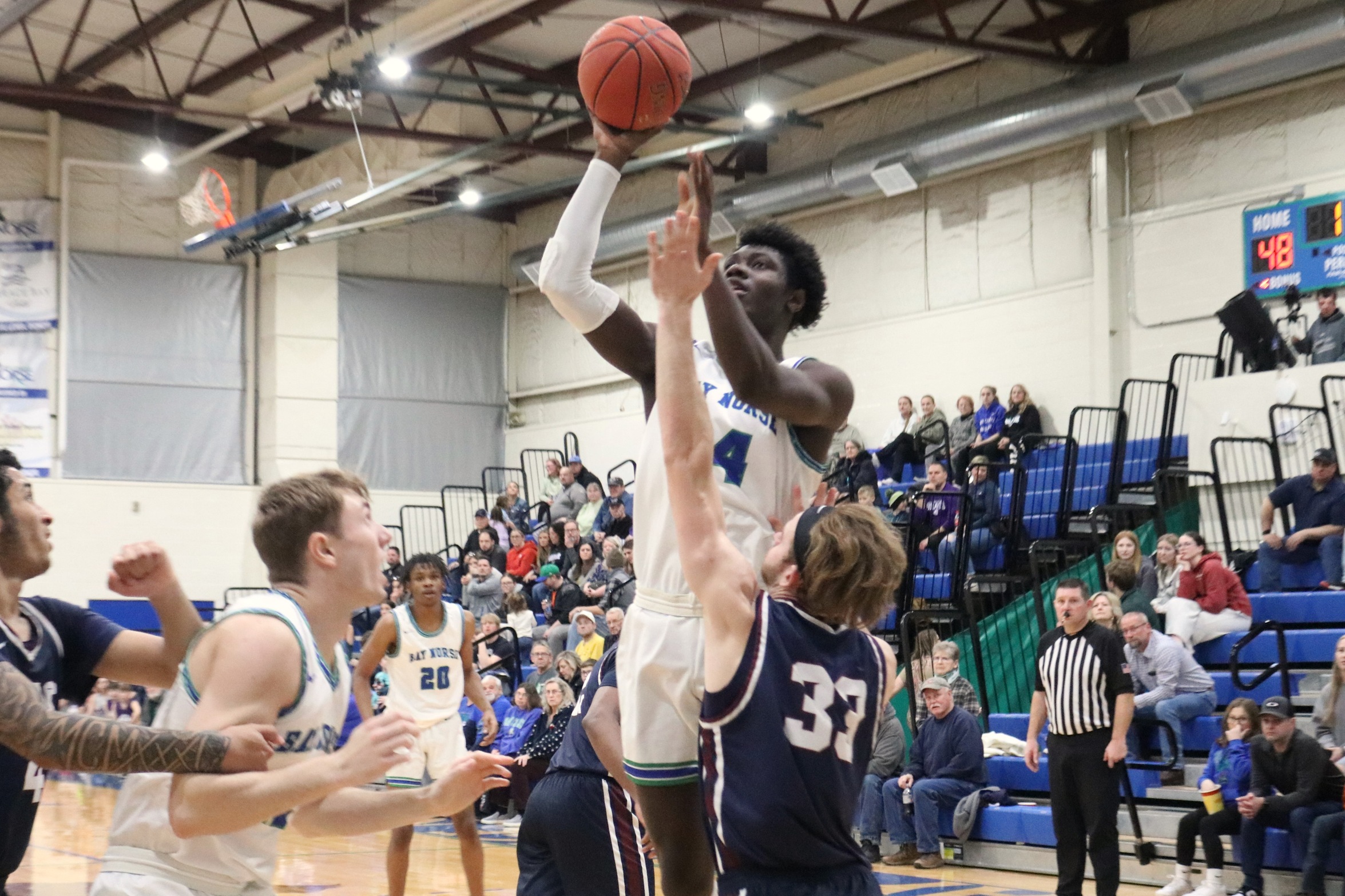Joshua Ofori jumps in the air, about to release a shot in the lane.  A defender has a hand stretched up, Ryan Sweeney looks on besides Joshua.