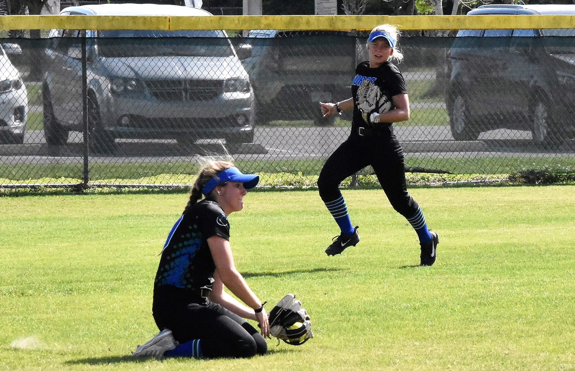 Jerricka McAlpine sliding on her knees and making a catch in the outfield as Emily Bruntjens watches in the background