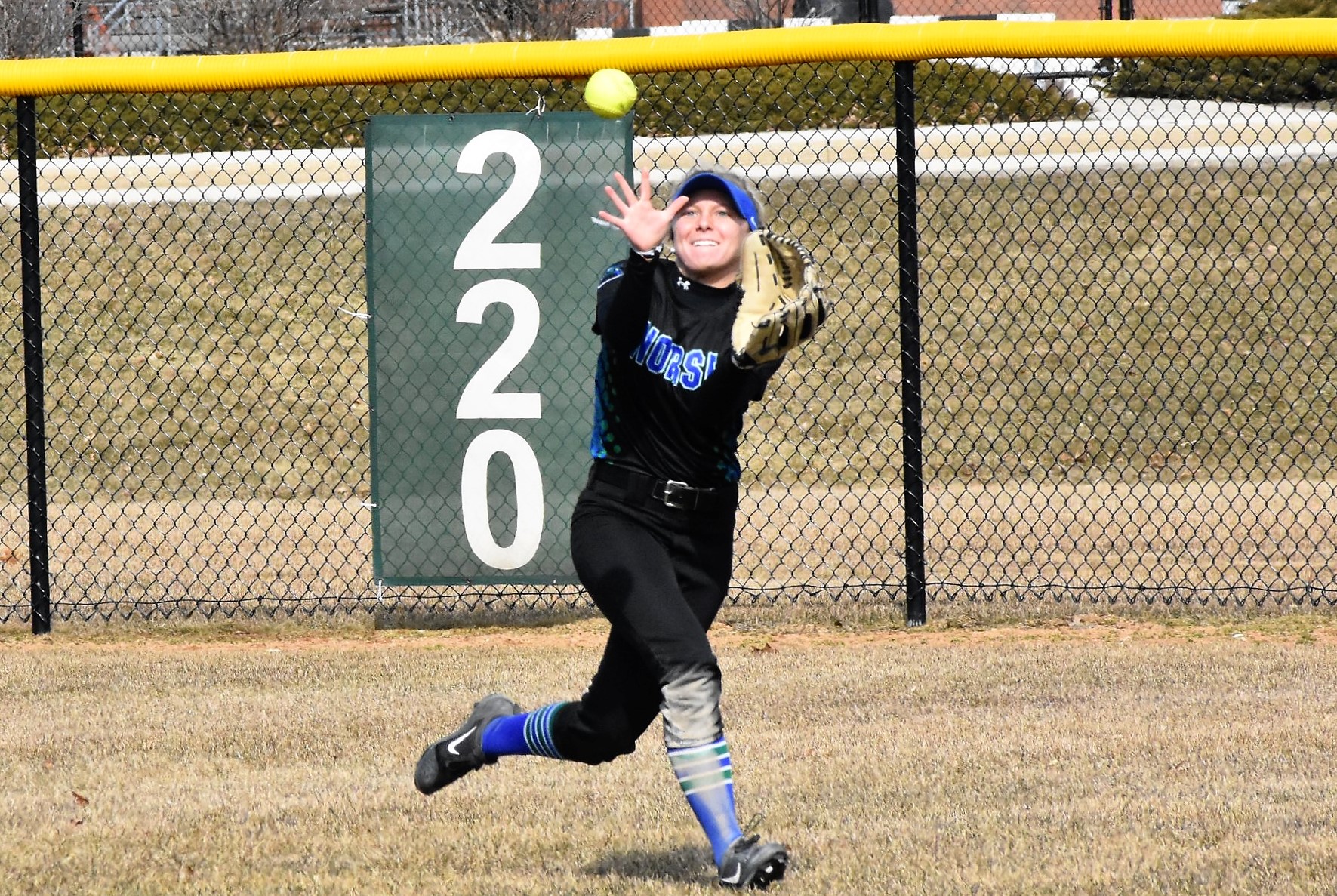 Emily Bruntjens reaching out to make a catch on the run near the 220 sign on the outfield fence