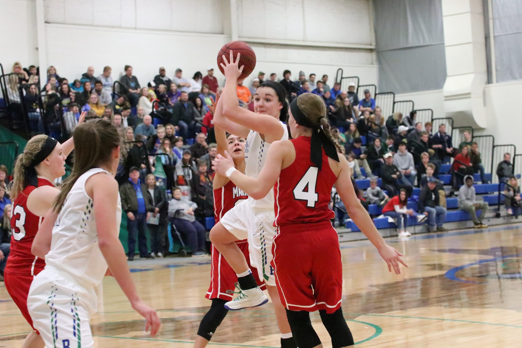 Taylor Hunter jumping in between two defenders.  She is holding the ball above her head looking to her left for a pass