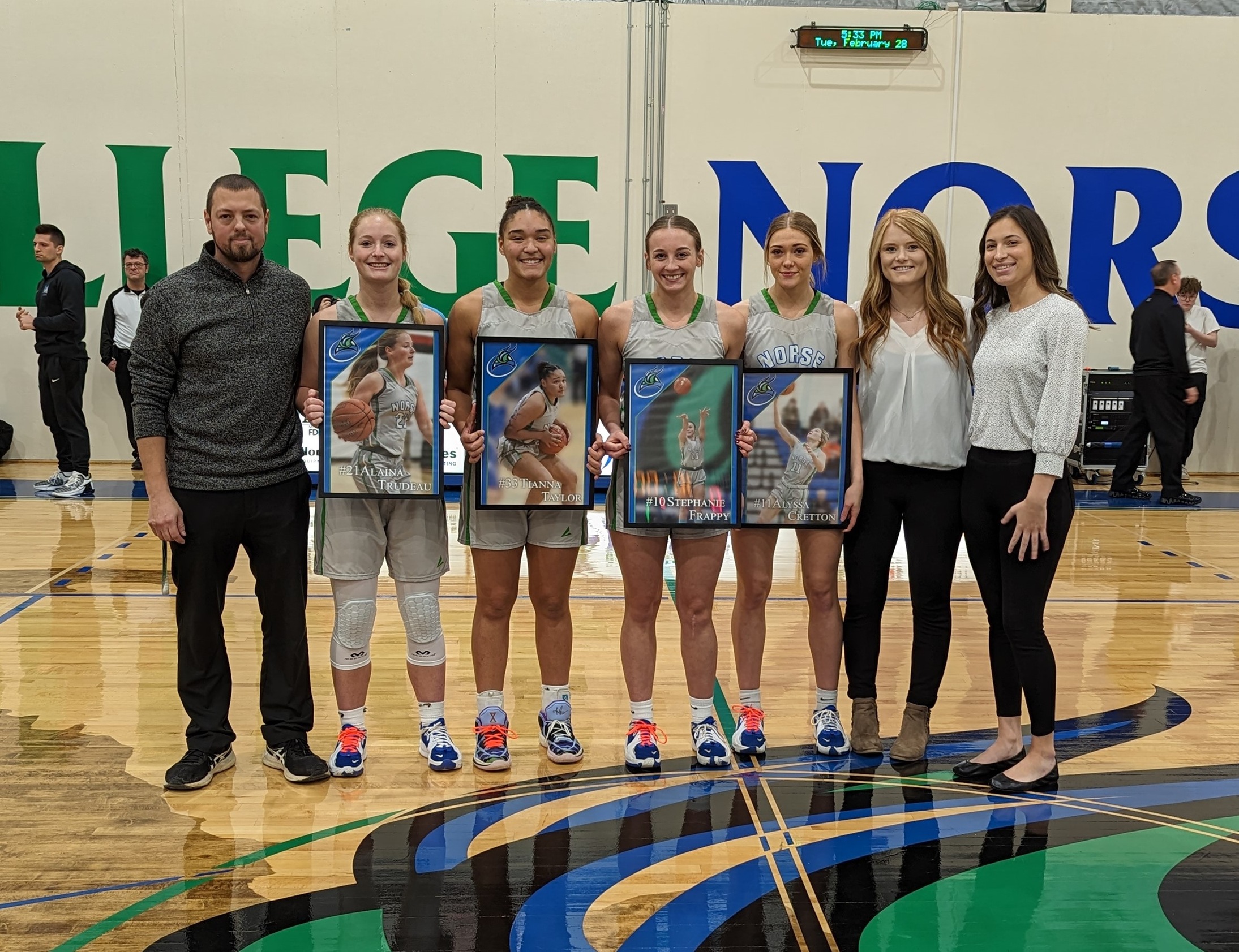 Matt Gregory, Alaina Trudeau, Tianna Taylor, Stephanie Frappy, Alyssa Cretton, Paige Welch, and Kennedy Englund pose at half court, the sophomores show their pictures given as gifts accompanied by the coaching staff.