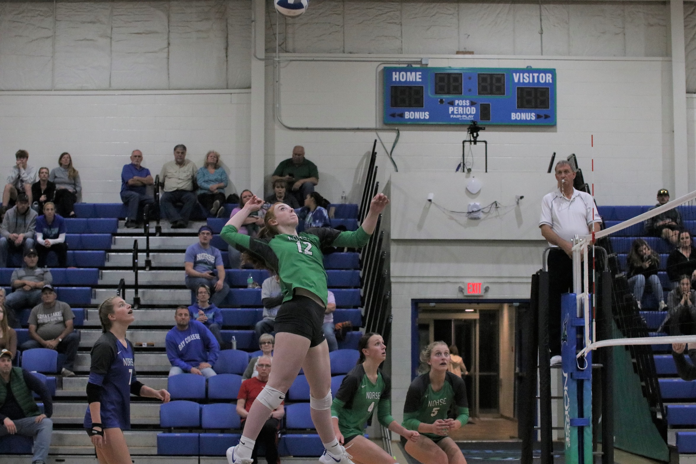 Kylee Tadisch in the air, about to swing for a kill as her teammates look on