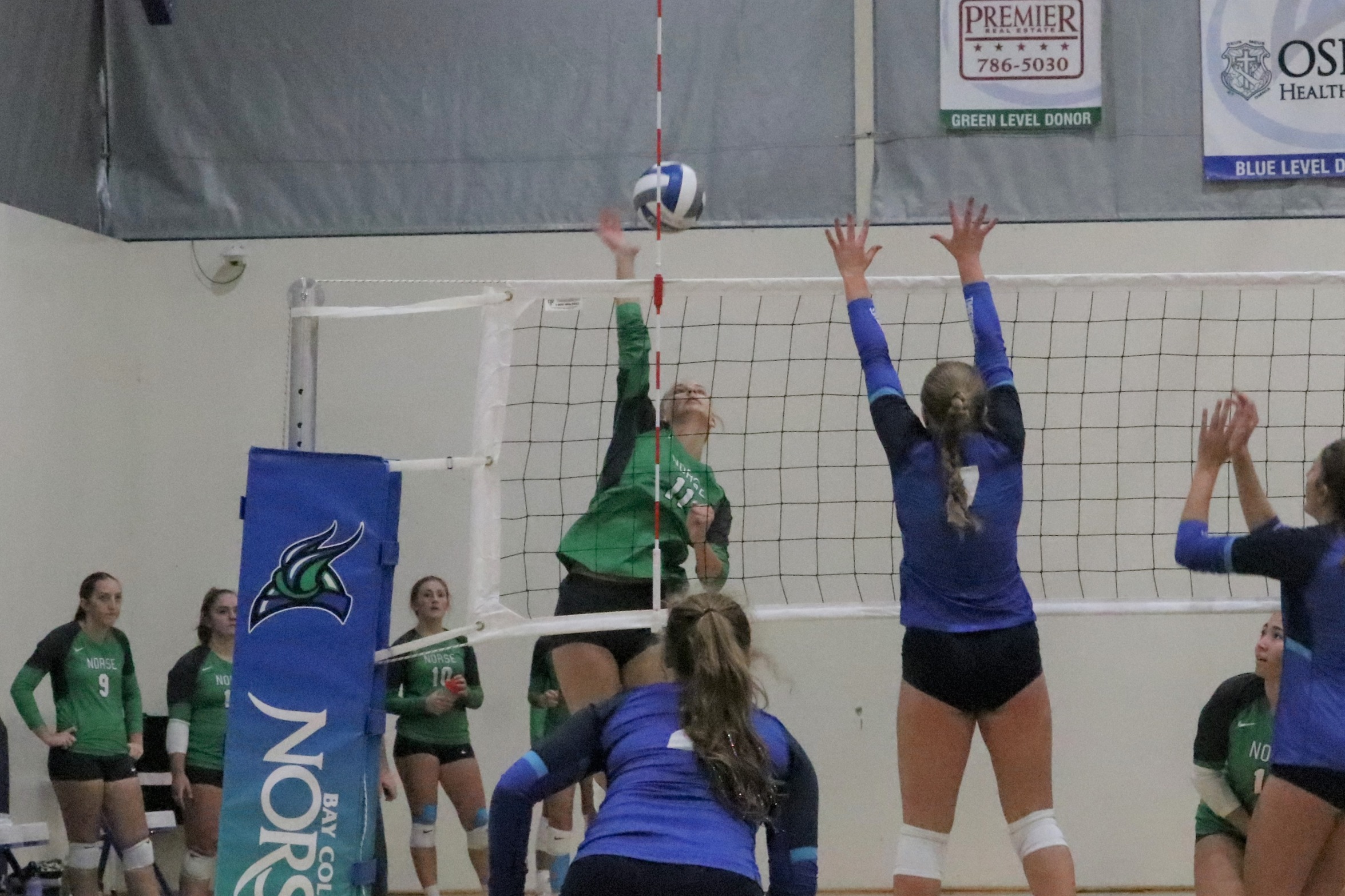 Olyivia Saxton in the air, swinging for a kill as an opponent leaps to attempt to block